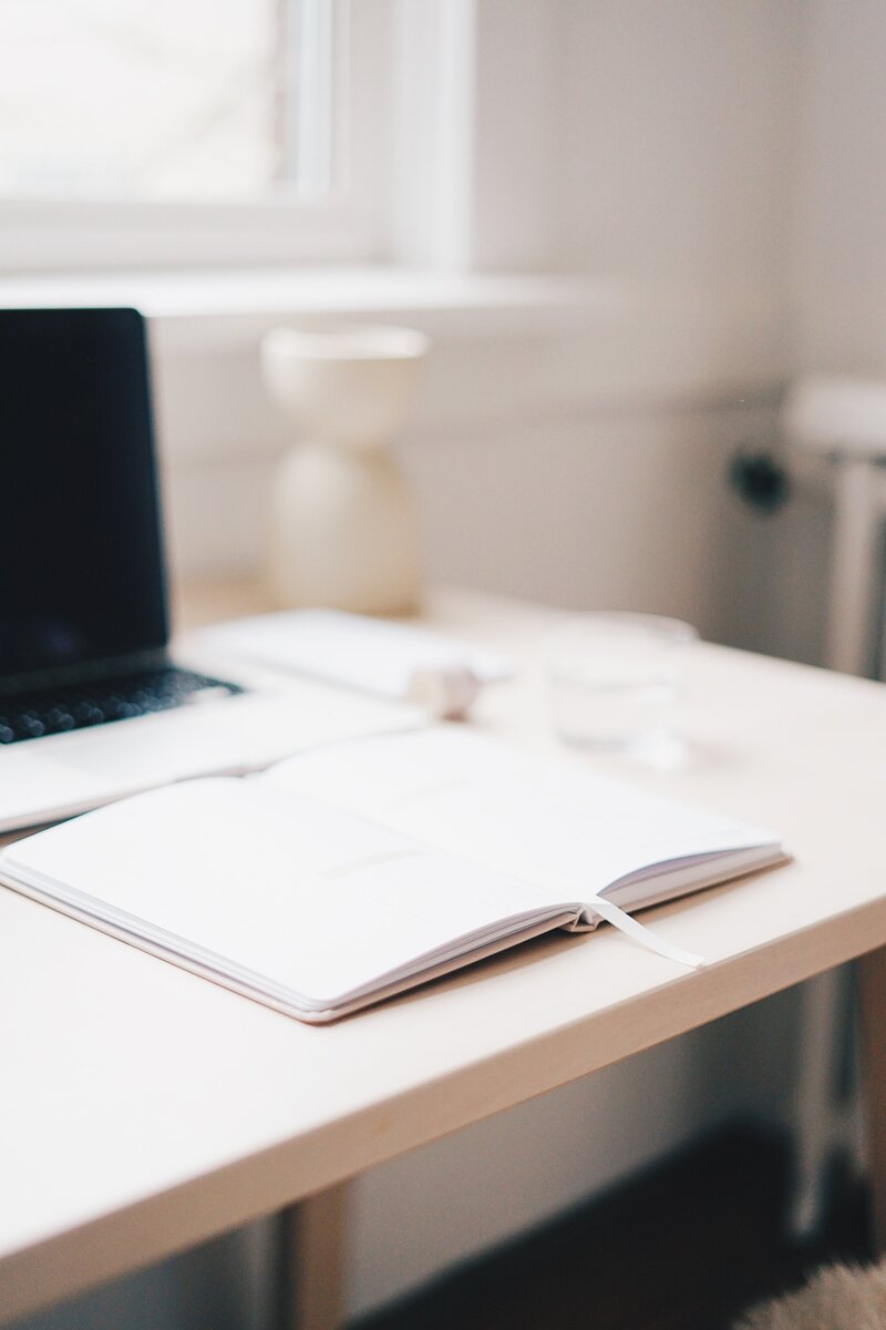 a blank notebook lies open in front of a laptop