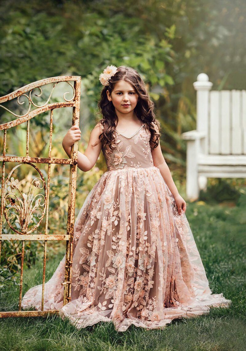 Young girl poses by a metal gate in beautiful lace dress