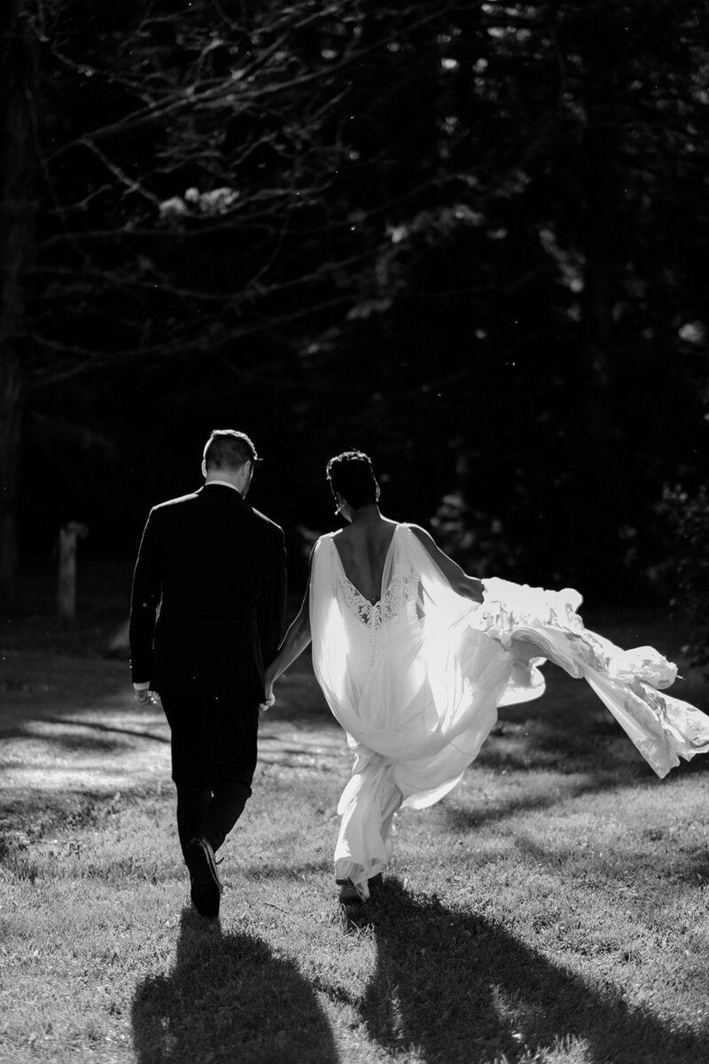 Couple strolls in forest, bride’s gown trailing, serene shot.