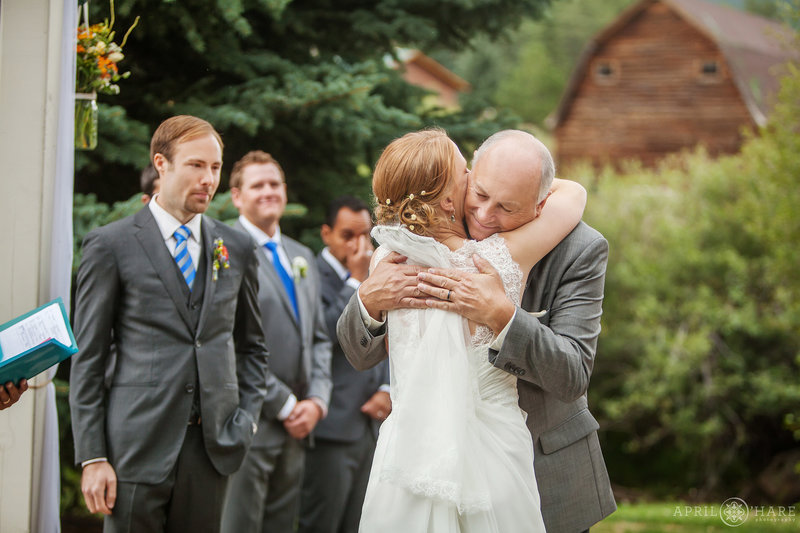 Bride hugs dad at her outdoor Colorado mountain wedding ceremony with a barn
