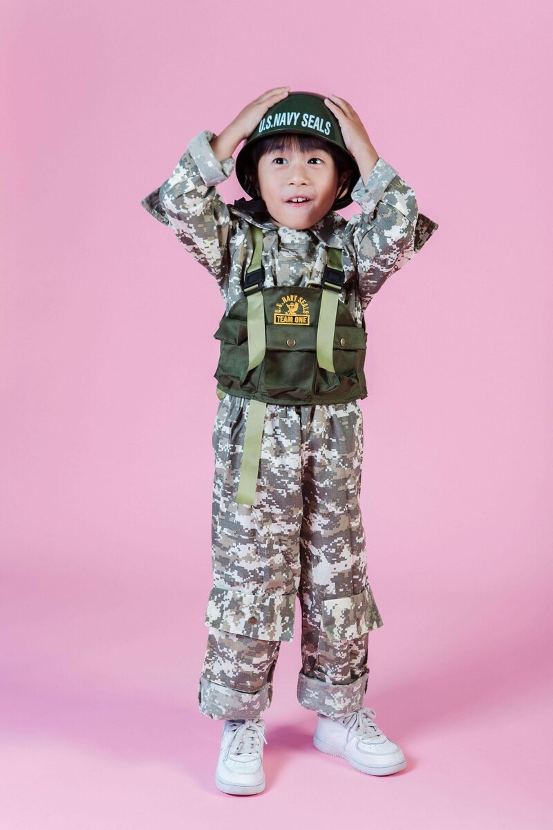 a young child standing against a pink background wearing a military-inspired costume