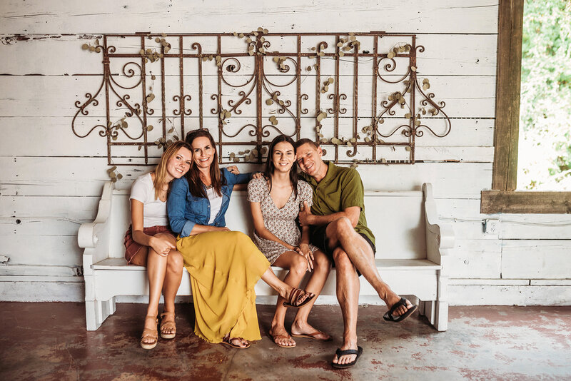 mom, dad and 2 teen daughters sitting together on a bench in a studio.