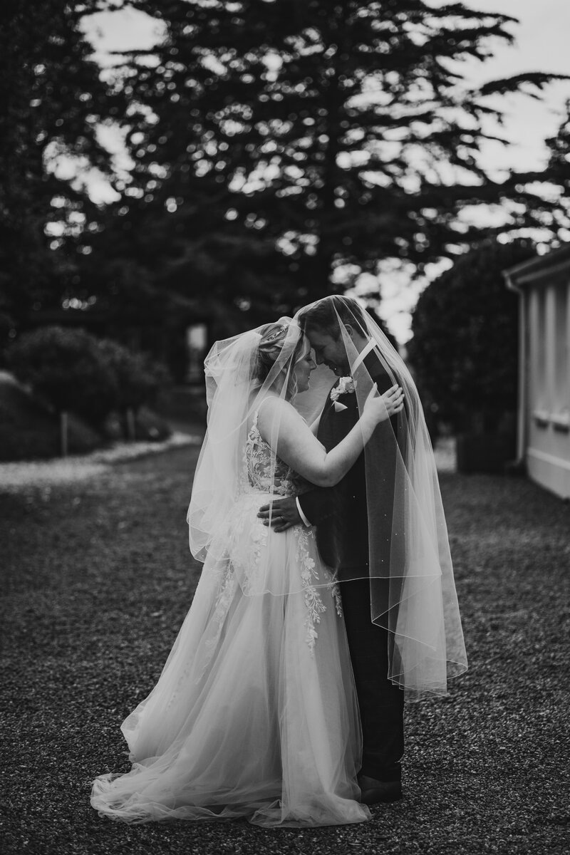 black and white photo of bride and groom under veil