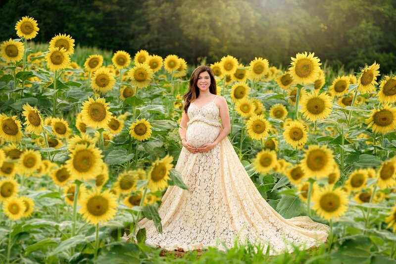 expectant mother standin gin a sunflower field wearing a boho cream dress
