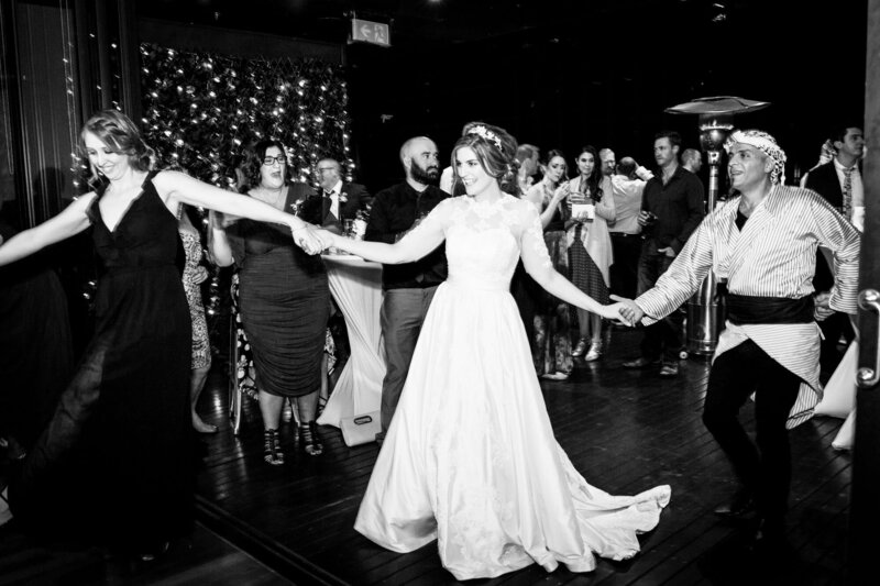 Bride holding hands while dancing with friends at wedding reception