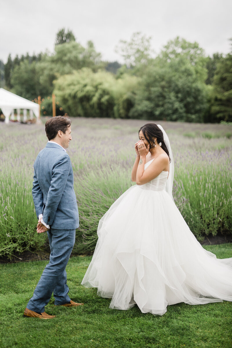 bride viewing her groom for the first time on her wedding day and tearing up with emotions. She is in a lavender field at a wedding venue in portland