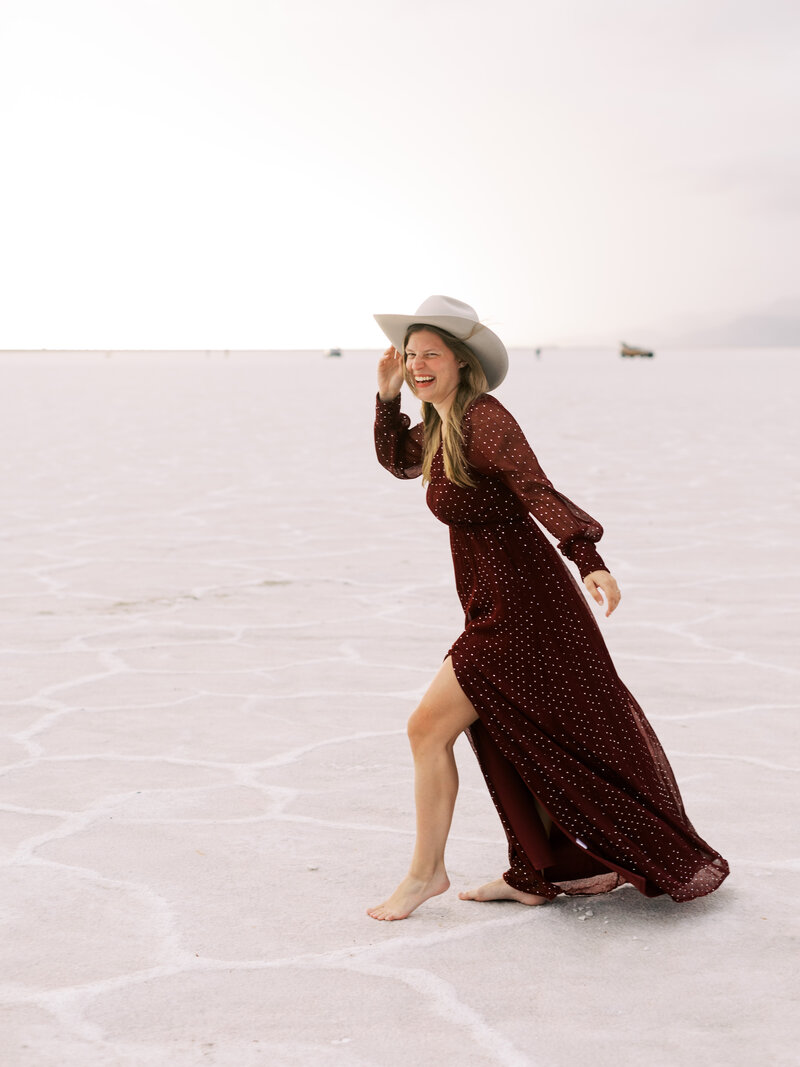 Destination wedding planner Skylar Caitlin walks on the Utah Salt Flats in a long dress and cowboy hat