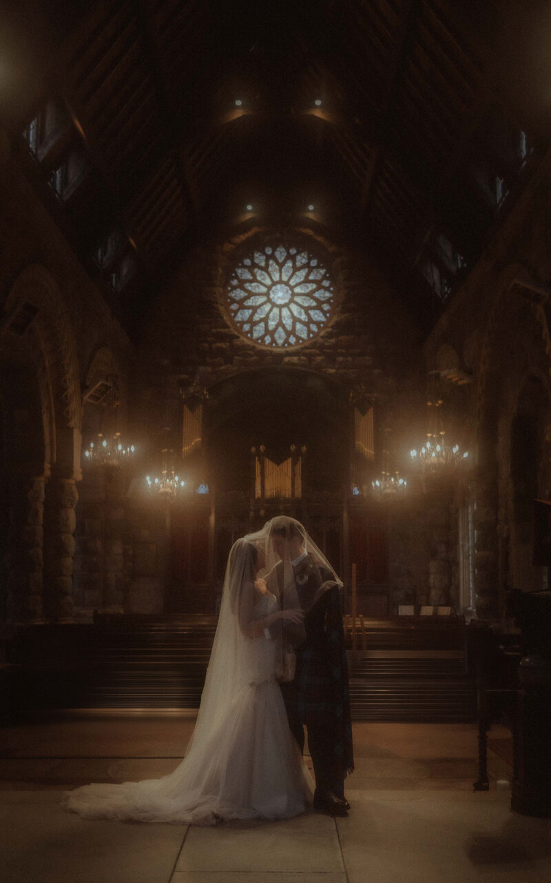 Romantic kiss between a couple under a veil in the serene St. Kirk Church, capturing an intimate and timeless wedding moment surrounded by sacred beauty