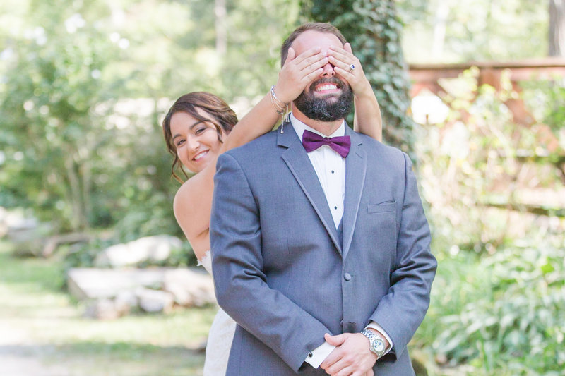 Bride smiles while covering her groom's eyes from behind on their wedding day