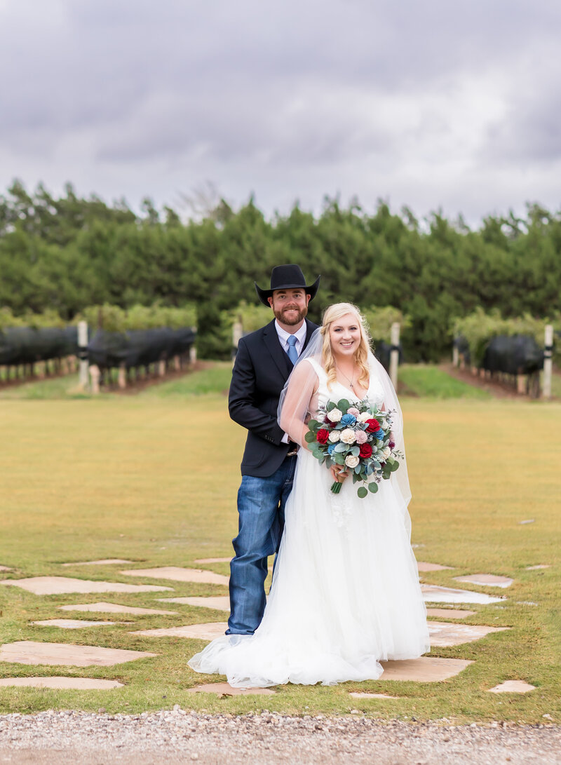 Bride and groom standing in a winery field holding bouquet