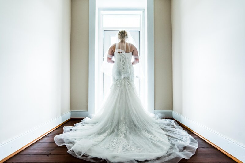 A bride poses in a white room for her wedding photographer in Austin, Michael T Davis, while looking out the window, showing off her wedding dress