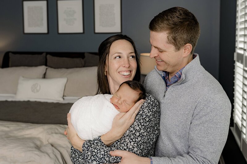 Charlotte Area mother holds newborn son and her arms while Dad stands beside her and they look towards each other