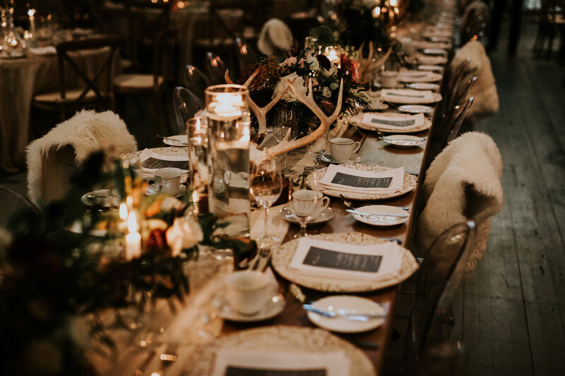 A moody and dramatic harvest table featuring ghost chairs, sheepskin blankets, skulls, candles and flowers for a wedding at a converted church called AllSaints in Ottawa Ontario