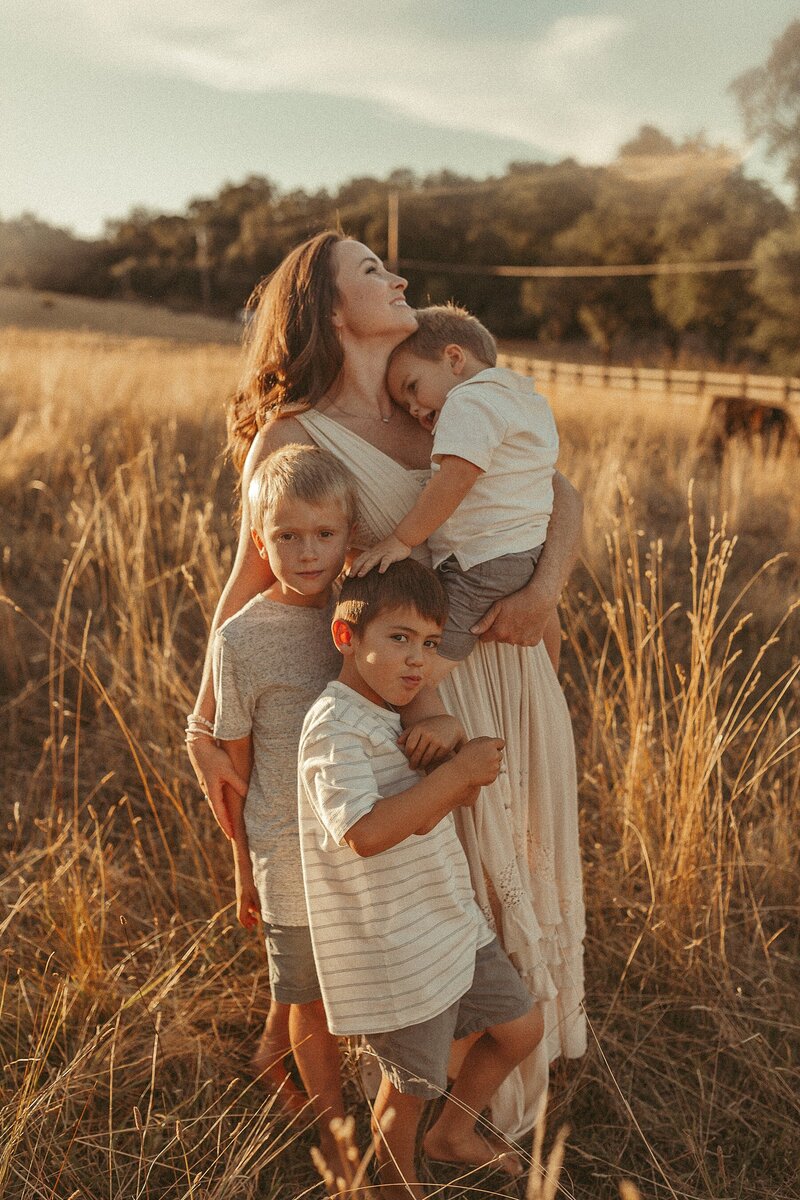 A woman holding her children in a field at sunset.