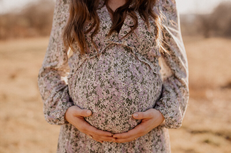 Schwangere hält Babybauch bei natürlichem Outdoor-Shooting liebevoll in beiden Händen