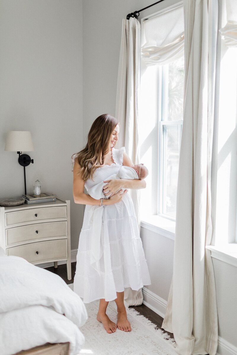 mother holding newborn baby near sun soaked windows by Orlando newborn photographer