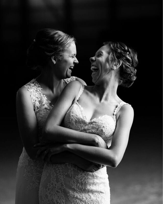 two brides in white dresses hug and laugh