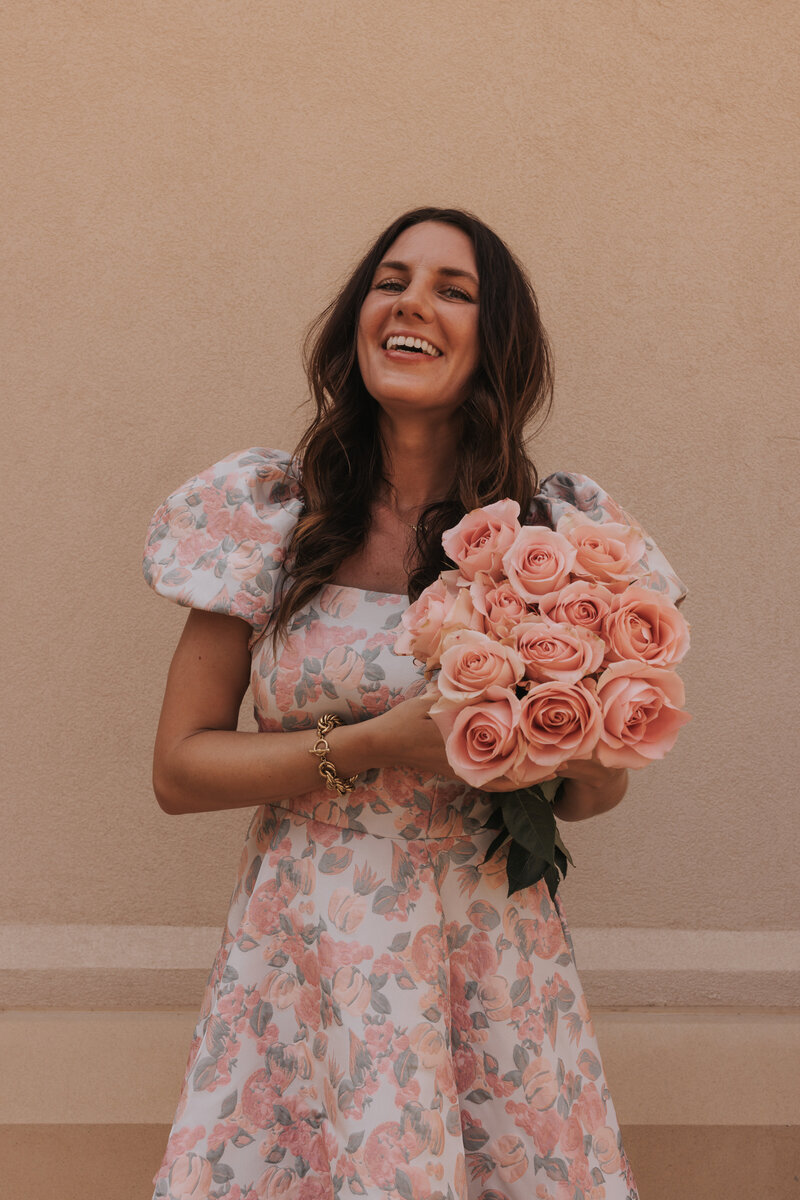 Claire in a pink floral dress holding a pink rose bouquet
