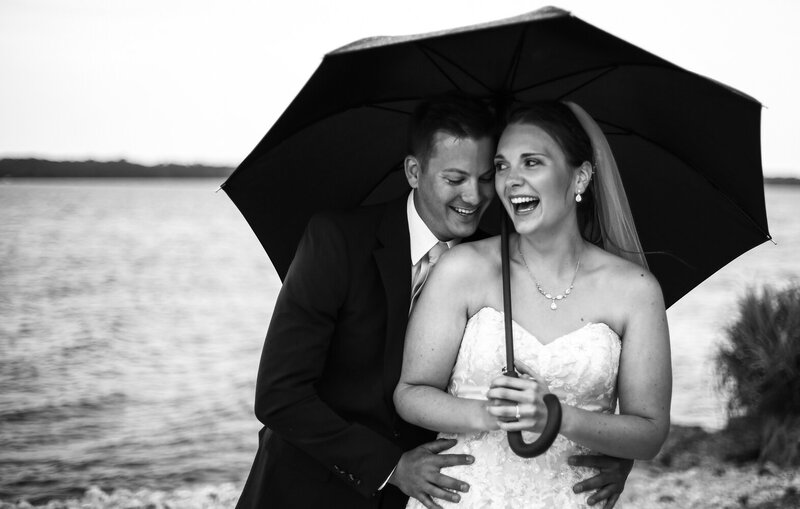 Laughing bride and groom stand under an umbrella at the Erie Yacht Club
