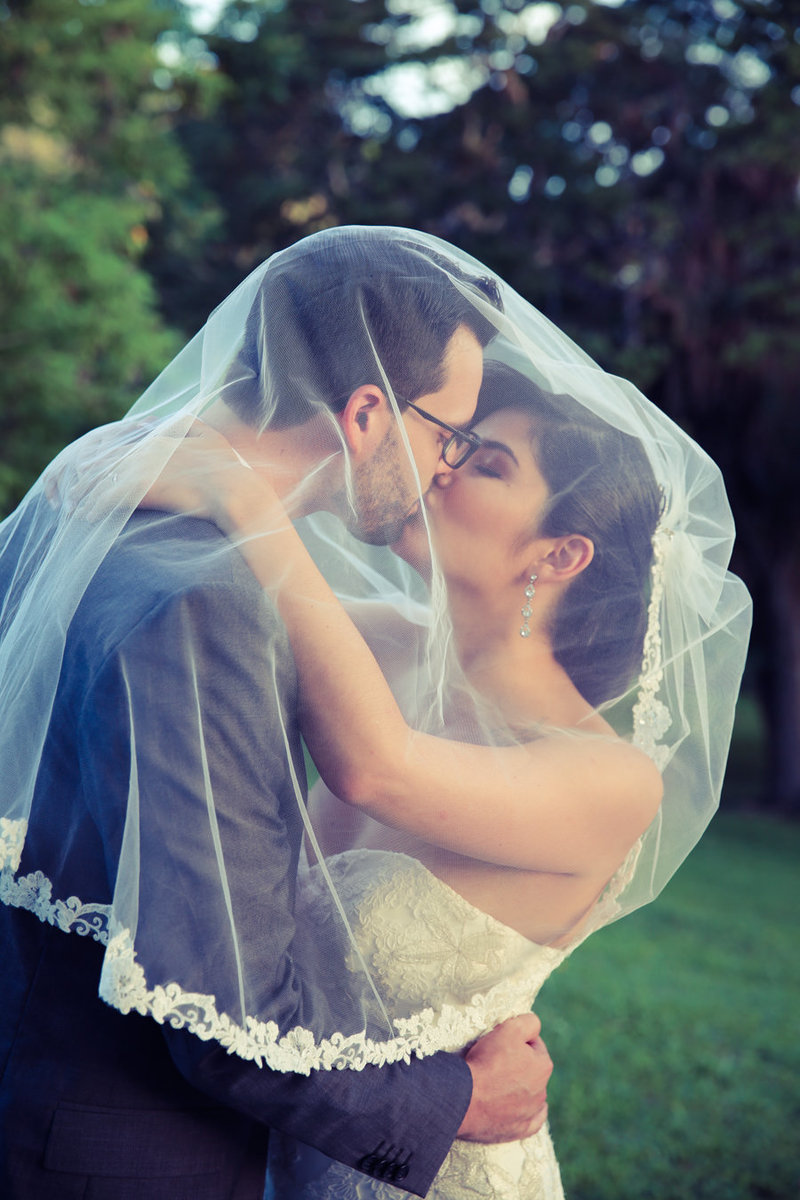 Bride and Groom kiss while wrapped under veil.