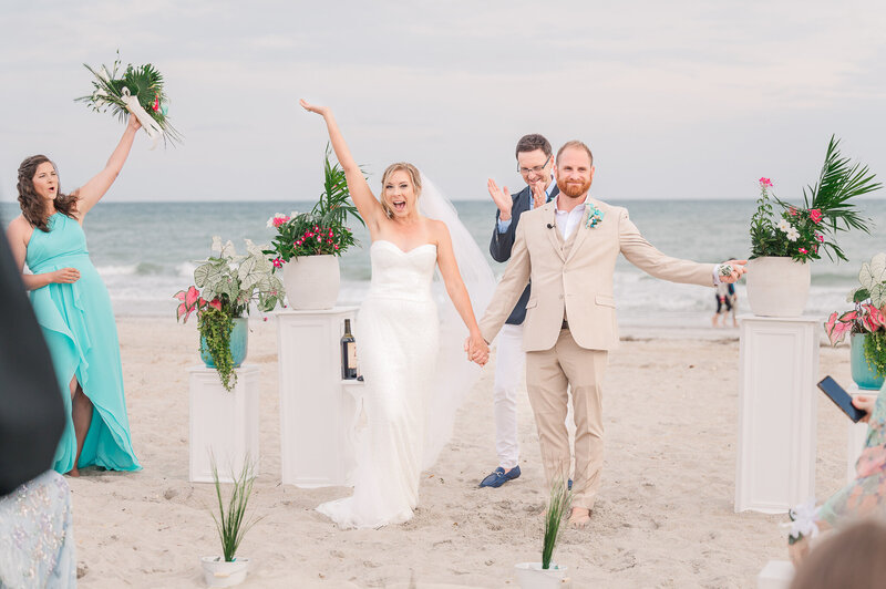 An excited bride and groom after saying I-do on the beaches of Wilmington celebrating with their friends and family as their Wilmington wedding photographer, JoLynn Photography, captured it all