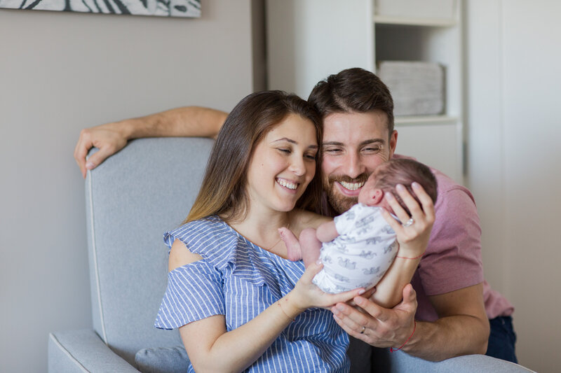 Mom and dad smiling at newborn holding in hands
