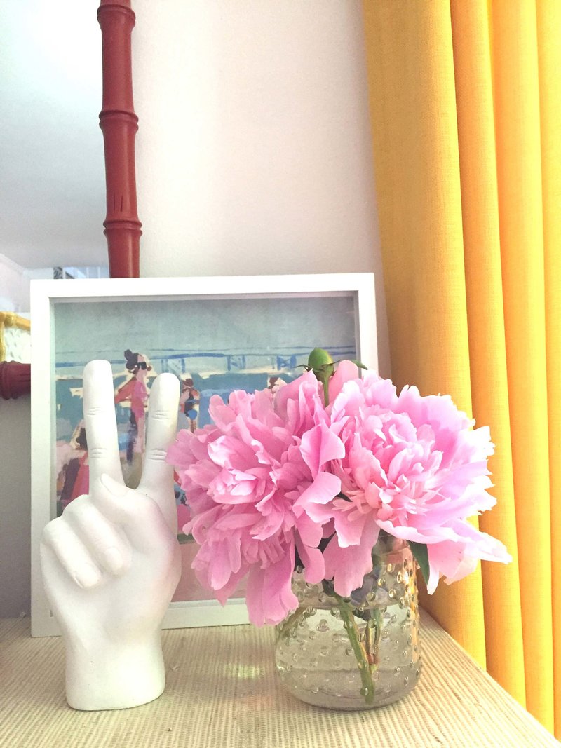 Pink flowers in a vase and  a ceramic peace sign hand on a table.