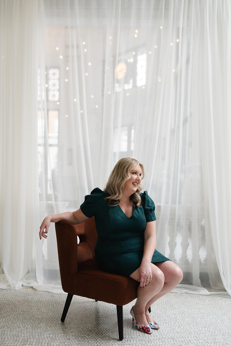 Leadership coach, Melissa Lawrence, sits in a velvet chair in a green dress and smiles
