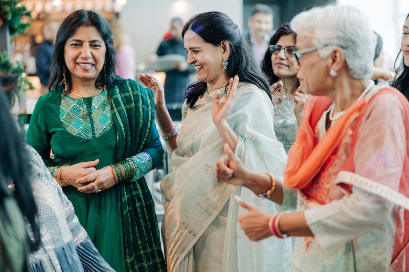 Women wearing Indian garments, dancing, and laughing.