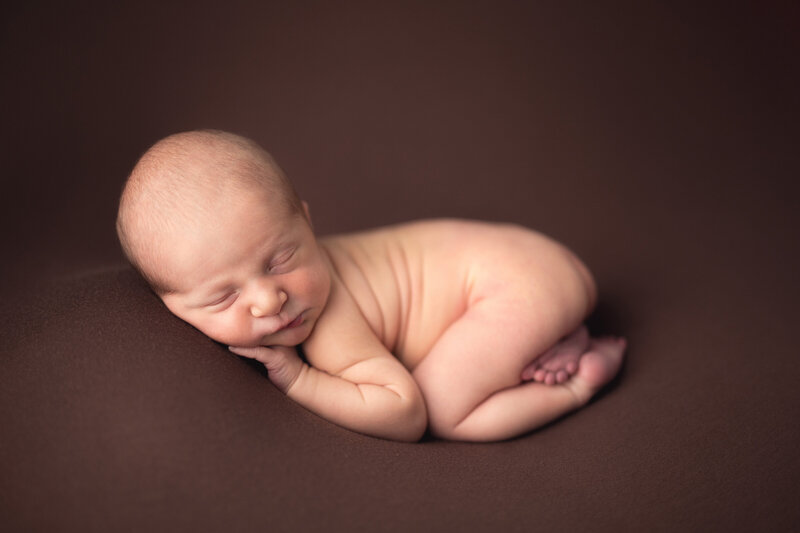 Sleeping newborn baby curled up on a brown blanket in Katie Lintern's Collingwood newborn photography studio