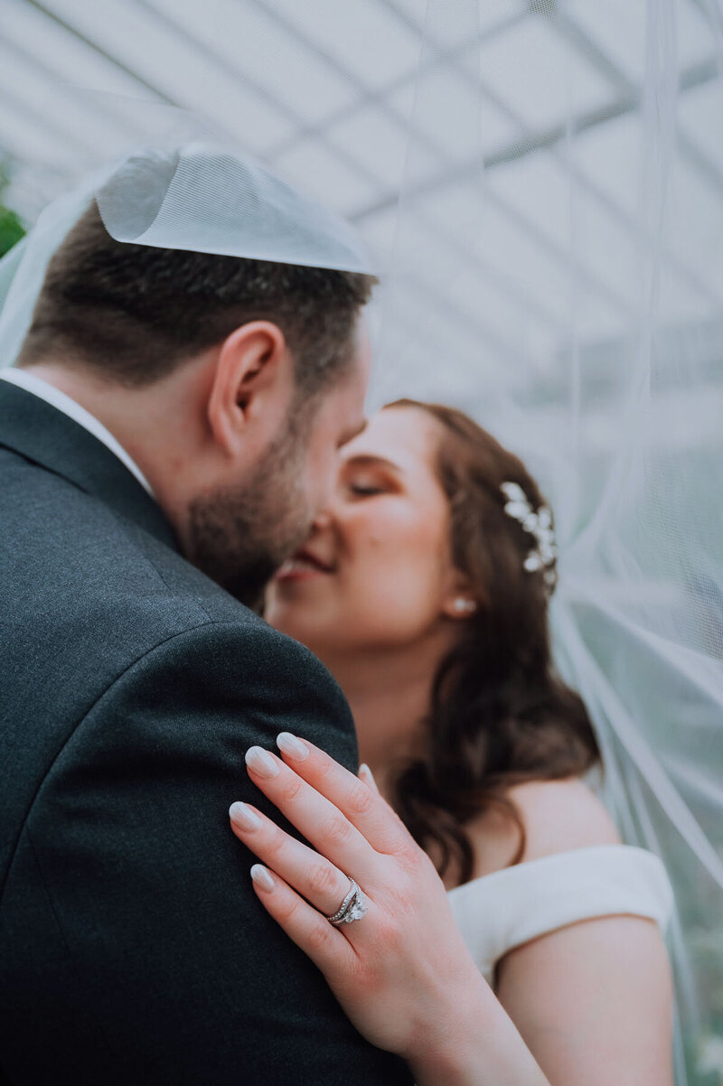 Bride and Groom kissing under bride's veil with photo focused on bride's ring