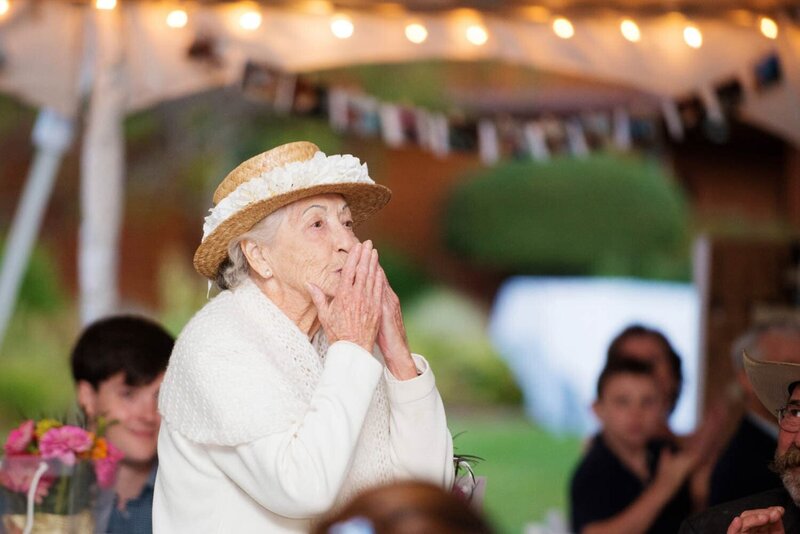 a grandmother kisses her hands to blow air kisses to the couple during the toasts
