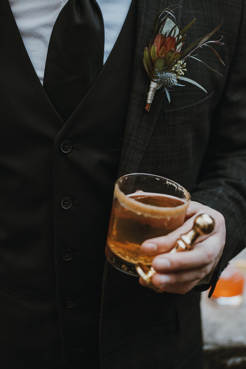 groom holding cocktail and ice stamper