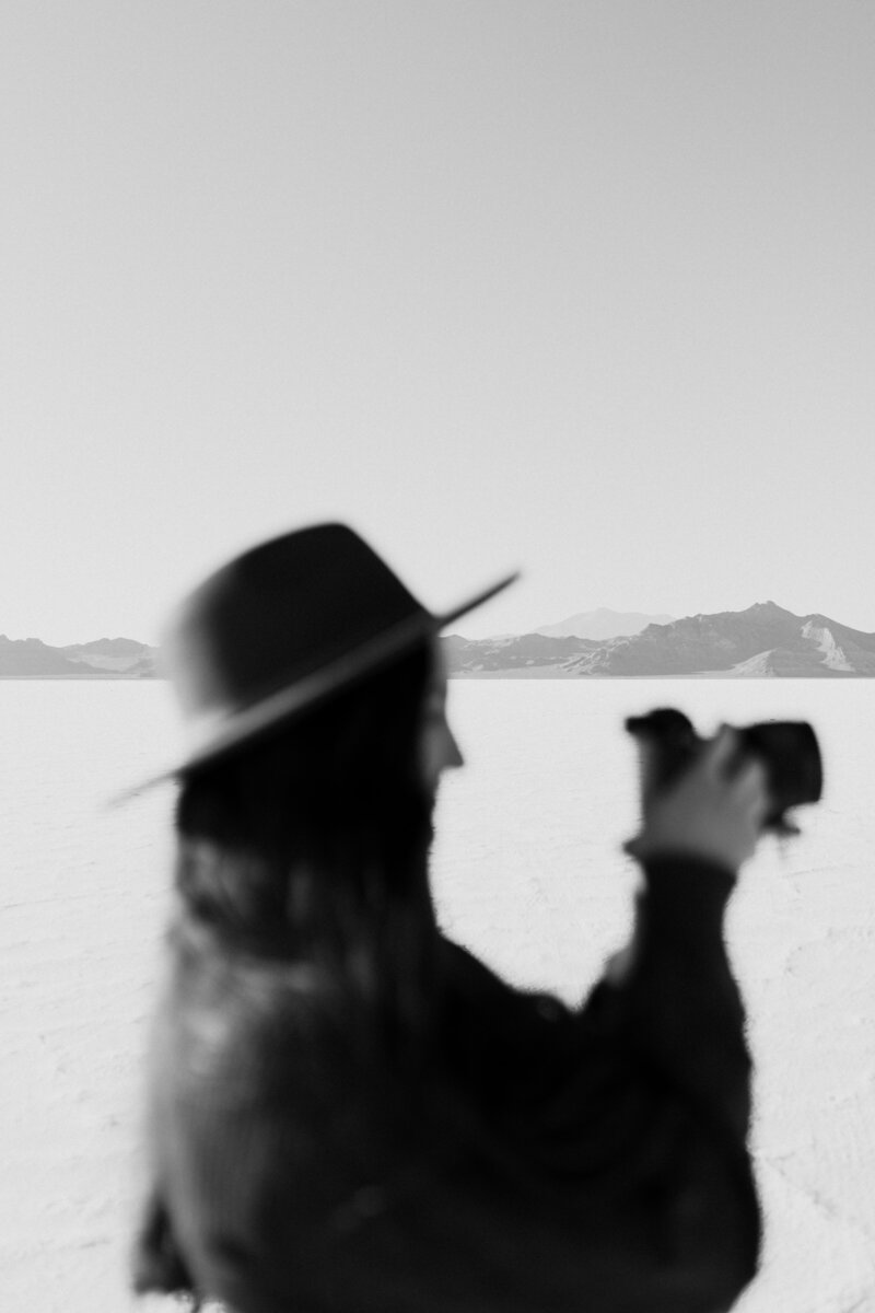 A stylish out of focus black and white photograph of Orlando Wedding Photographer Jo of Four Loves Photo and Films lining up a shot in the Salt Flats.