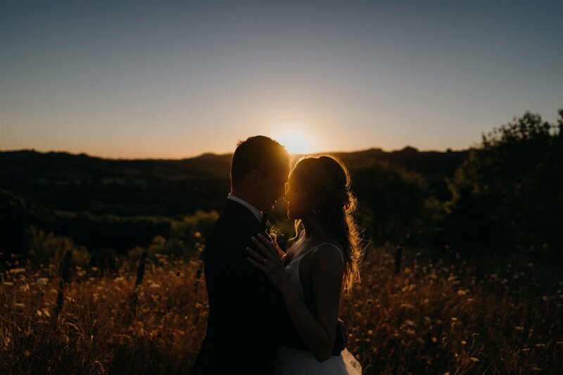 A bride and groom holding one another with the sunsetting in the background photographed by Tashina Narelle Photo + Video, an Auckland, Waikato and Tauranga Wedding Photographer and Videographer