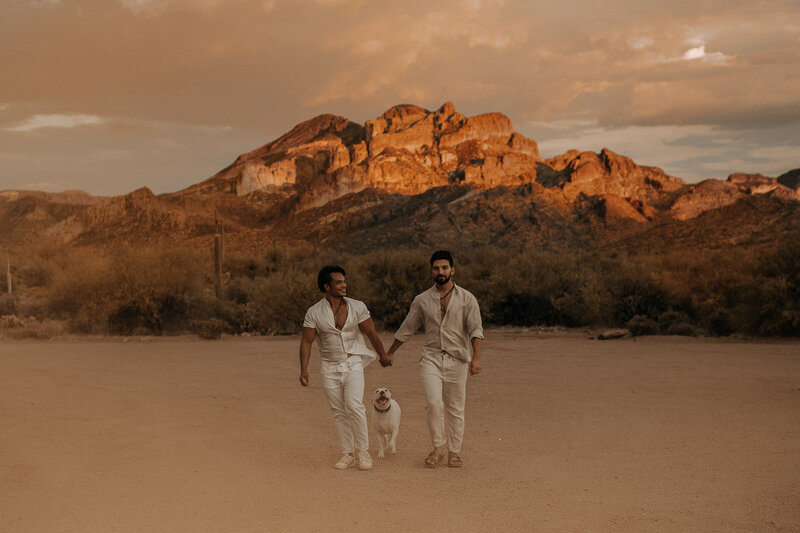 lgbtq couple engagement session walking towards camera at sunset with dog  in white linen outfit