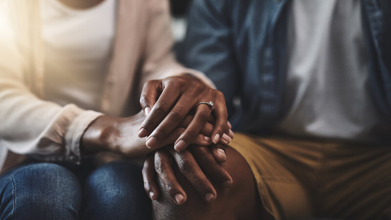 Black couple in therapy with hands stacked on each other, wedding ring on finger