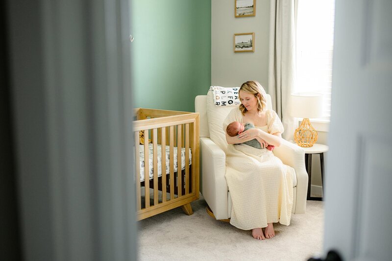 newborn is wrapped in cream being snuggled by his mother sitting in his nursery 
