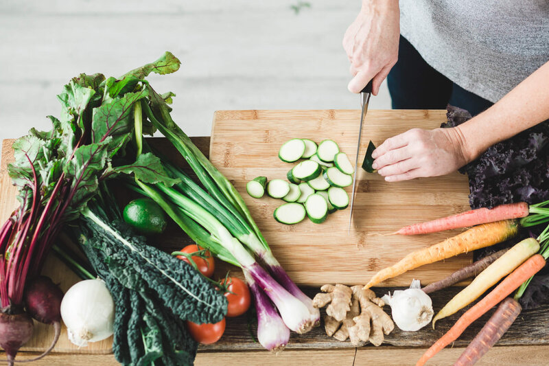 Picture of a cutting board and a woman chopping a variety of veggies. 