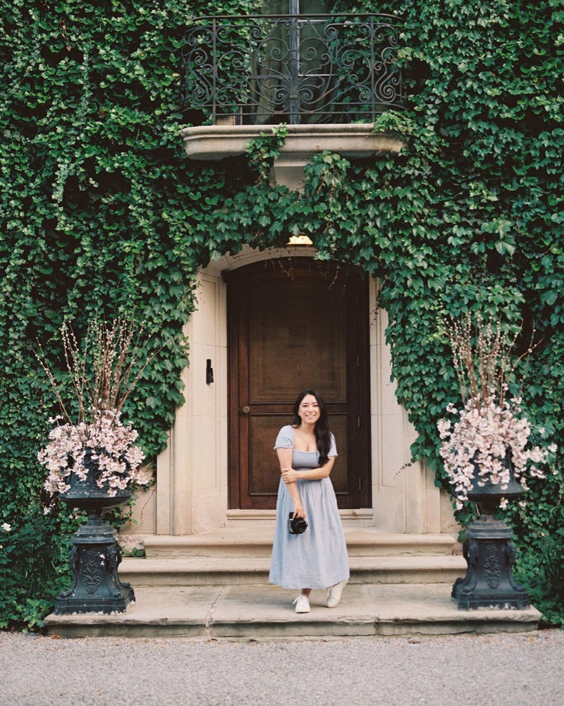 DFW wedding photographer Stephanie standing in front of Greencrest Manor wearing a pale blue dress and white sneakers