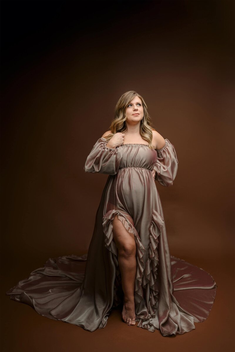 Charlotte area mom dressed in a brown and gold toned  off shoulder dress with dual leg slits on a brown background