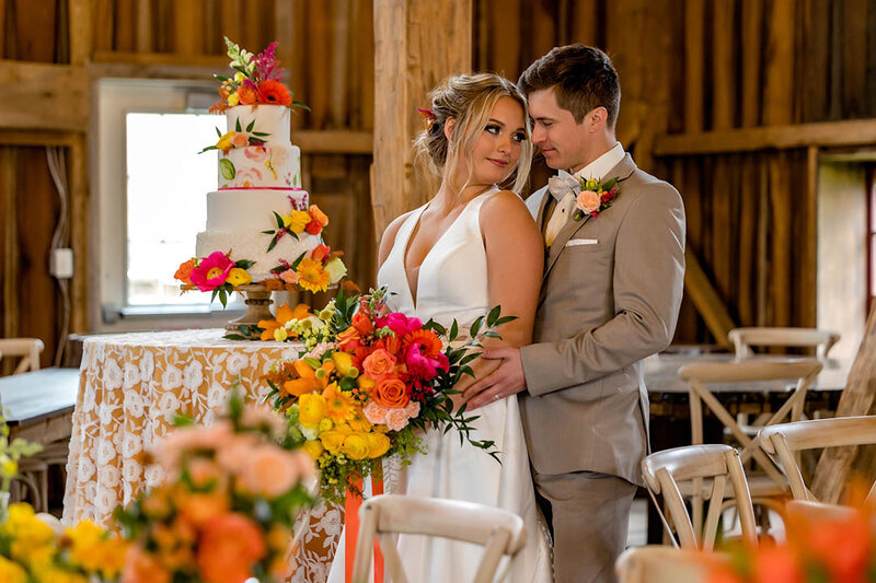 Bride and groom posing next to cake in the Country Strong barn