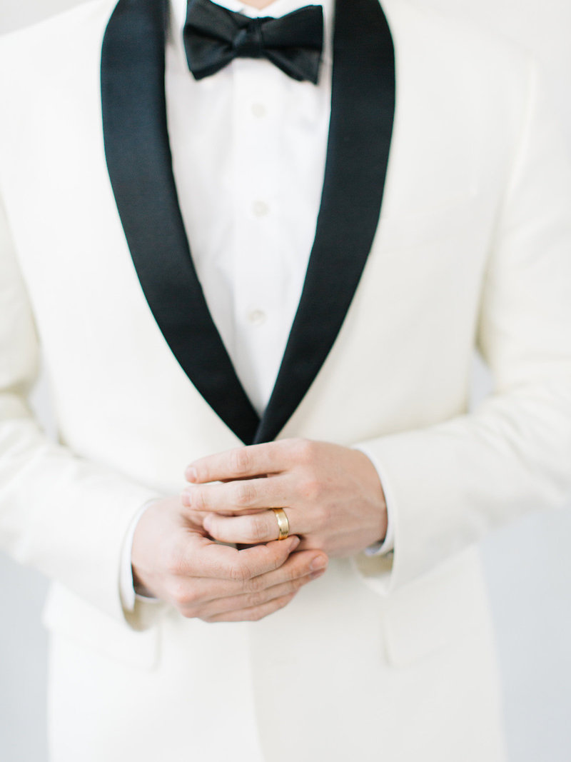 This groom is wearing a classic black and white dinner jacket holding an all white orchid bouquet