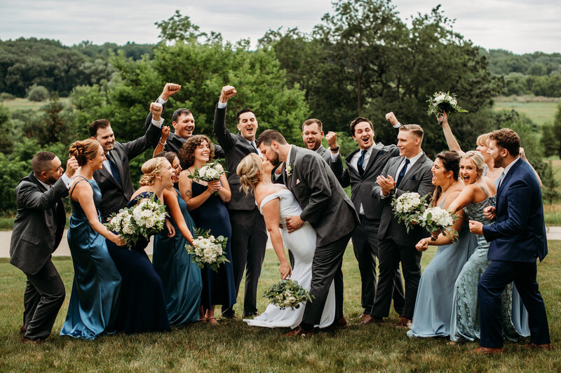 Bride and groom kissing while bridal party cheers for them