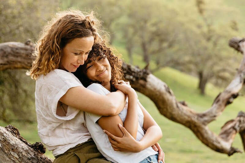 mother and daughter hugging while sitting on a large tree branch during a family video session  in san francisco