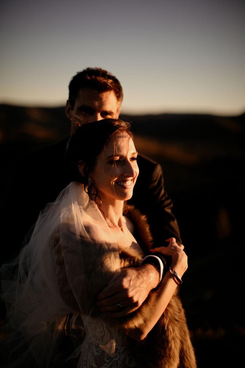 Wedding couple embracing each other as they watch the sunset in mountain view