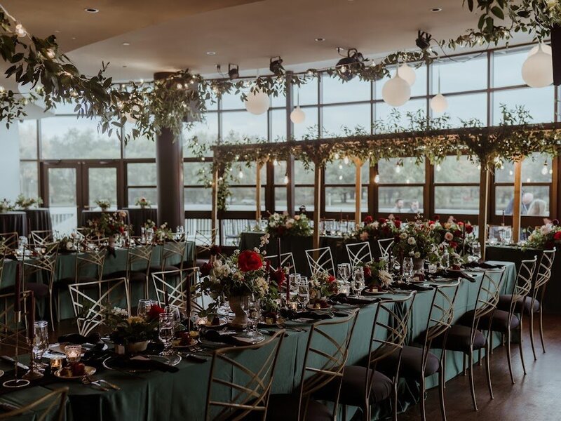 A sleek and moody wedding design at a Lago venue in Ottawa featuring forest green linens, burgundy flowers and a larger floral ceiling installation over the dance floor.