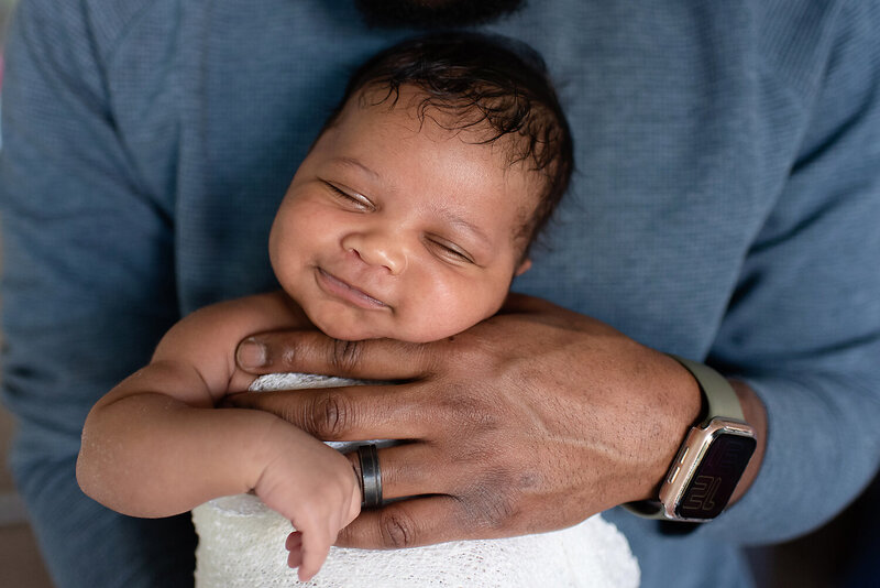 Smiling newborn boy sleeping in his father's hands