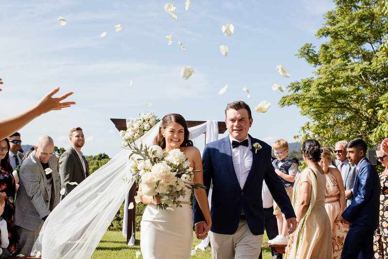 Guest throwing confetti over wedding couple while walking down the aisle