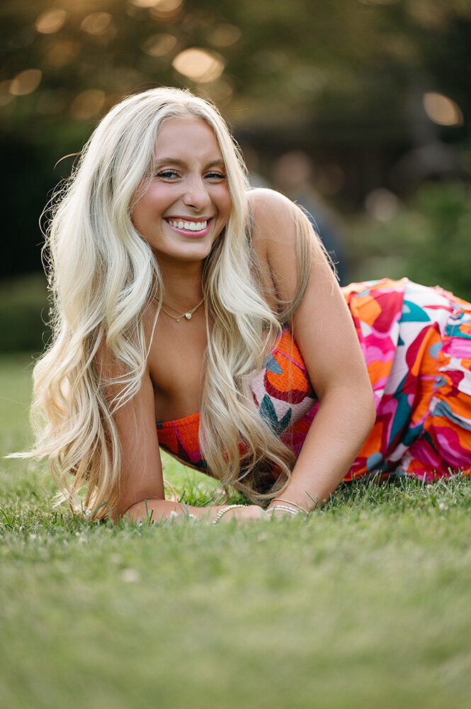 Blonde Senior laughs in the grass and a very colorful dress